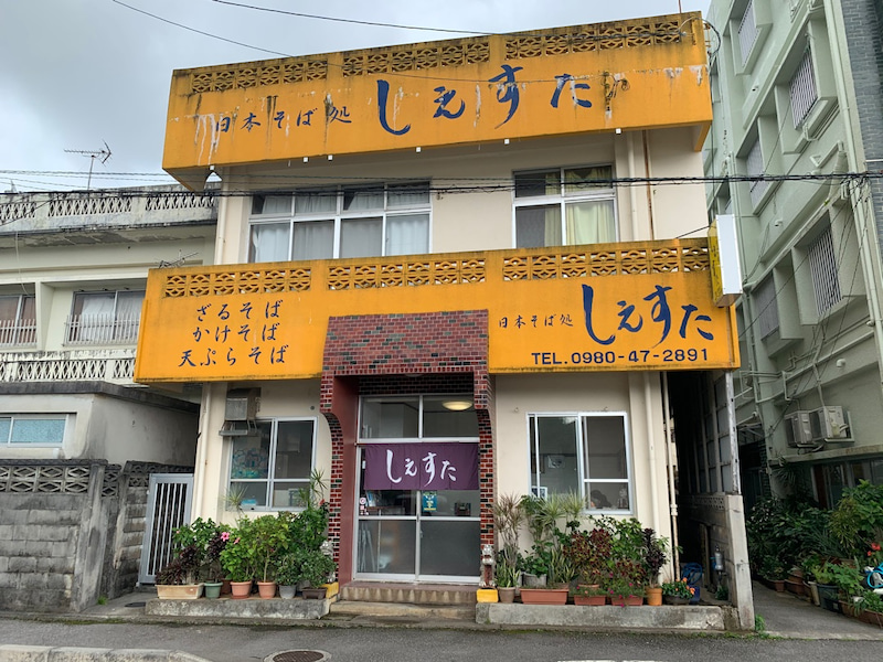 黄色い看板が目印の沖縄県本部町にある日本そば処しえすたの店舗外観