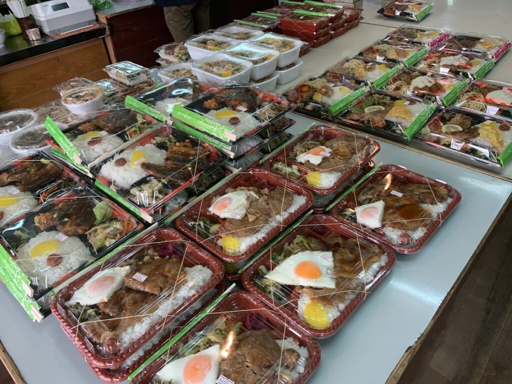 十八番の店内に並ぶ多種多様な沖縄弁当。ボリューム満点のおかずが見えます。