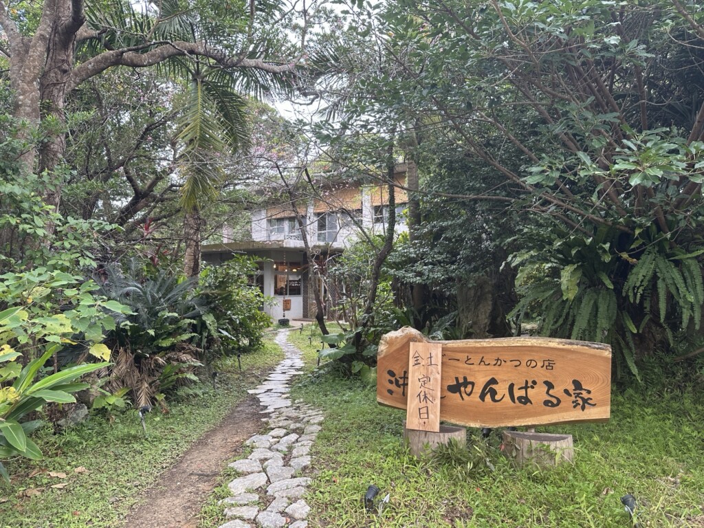 豊かな緑に囲まれた古民家風の「アグーとんかつの店 沖縄やんばる家」の外観と看板