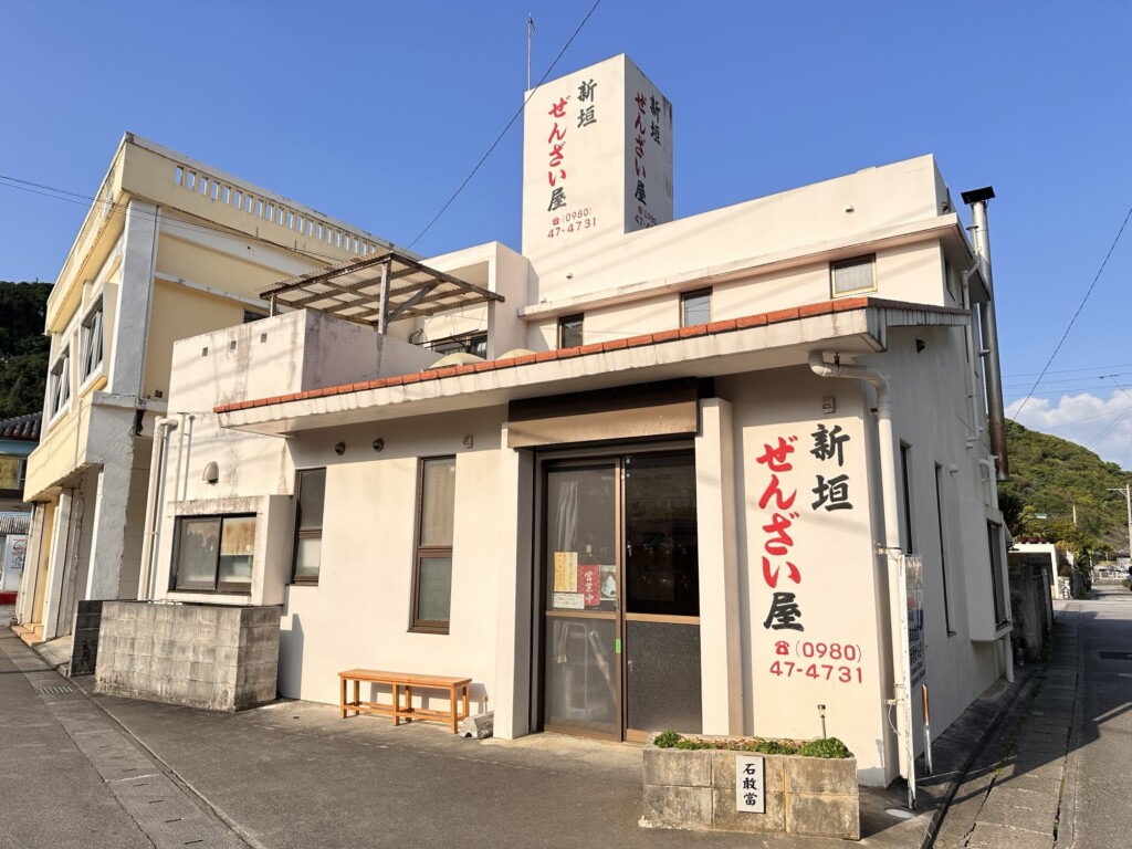 青い空に映える新垣ぜんざい屋の店舗外観。白い看板に大きく店名が書かれている
