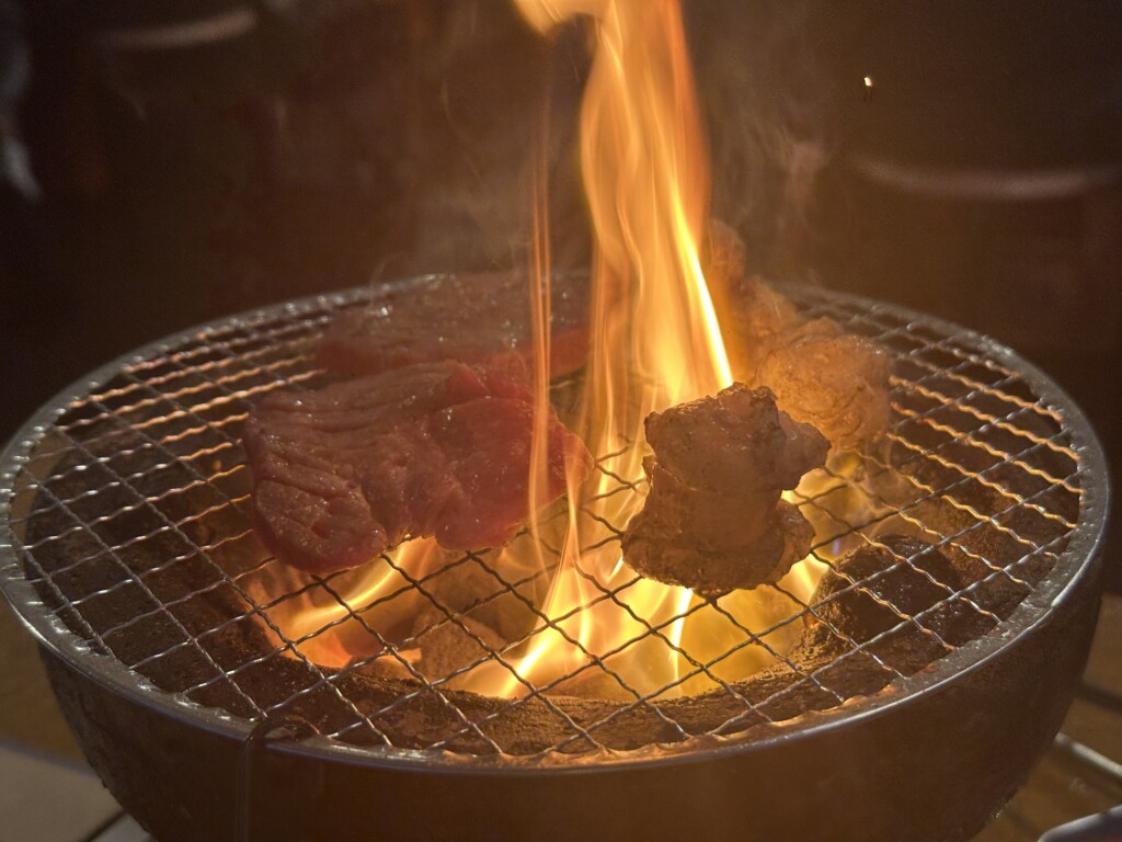 肉の脂が滴り、炭火から豪快な炎が上がるドラマチックな瞬間