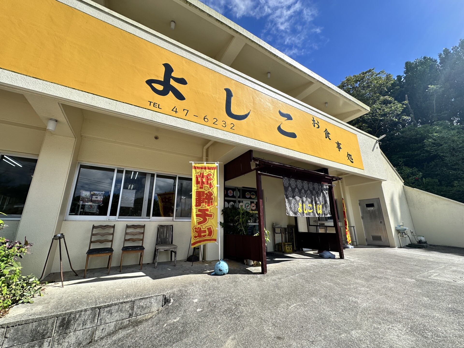 黄色い大きな看板と「よしこそば」の暖簾が掲げられたそば屋よしこの外観